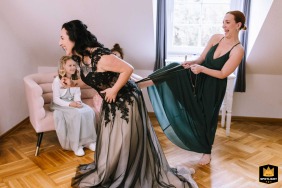 At Landgut Stüttem in Wipperfürth, a bridesmaid carefully adjusts the bride's dress, lending support during a quiet preparation moment before the ceremony begins there today.